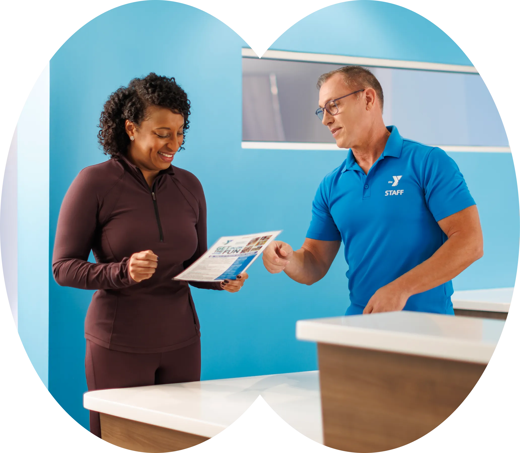 A YMCA staff member showing a tablet to a member at a welcome desk.