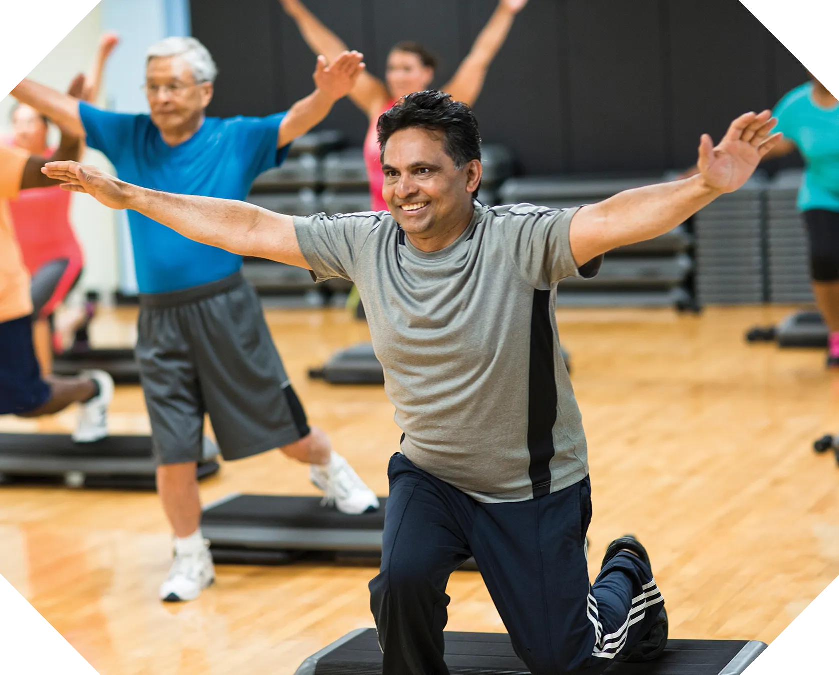 Two men exercising with arms outstretched in a YMCA fitness class.