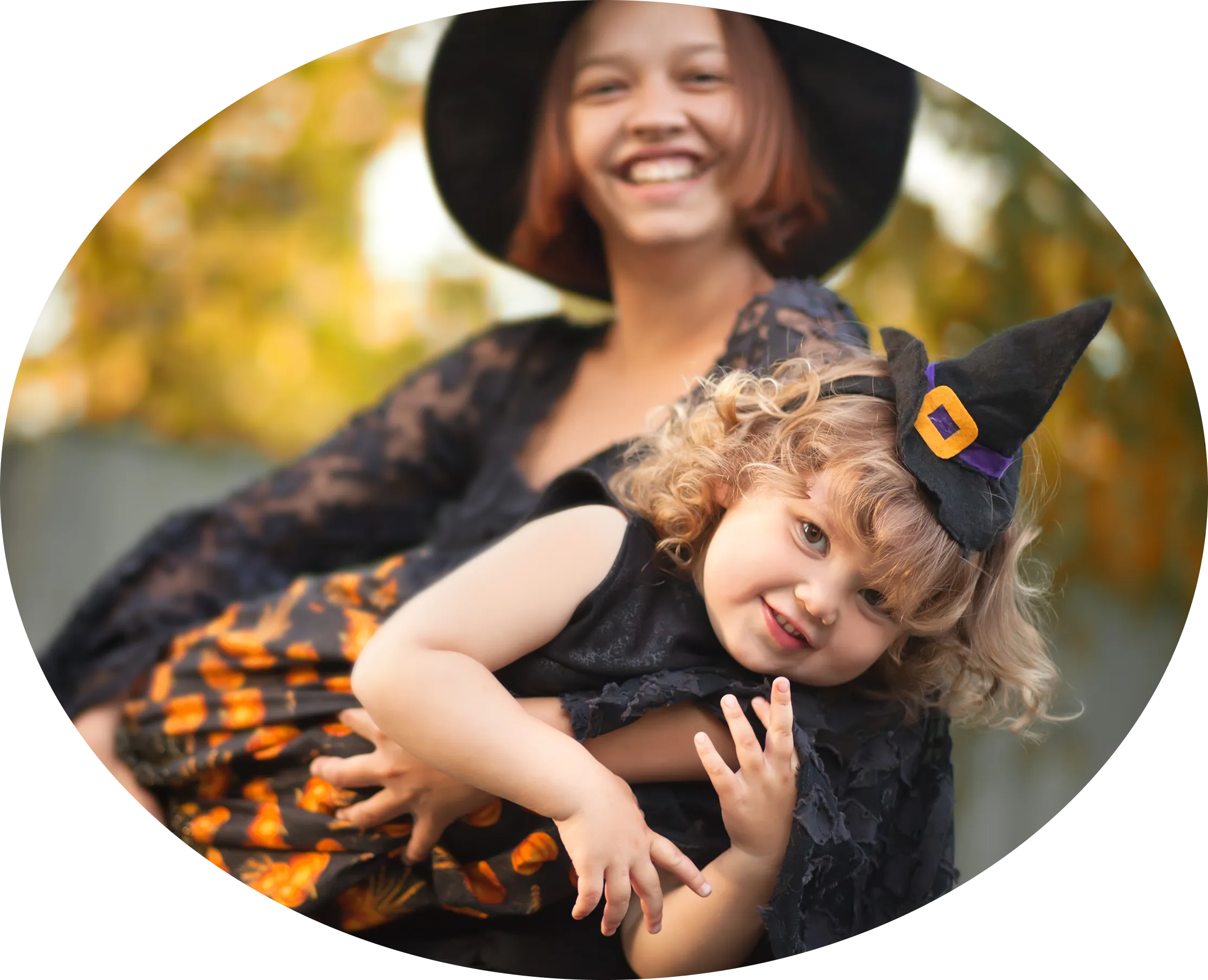 A parent holding a child in a witch's hat at an autumn family event.