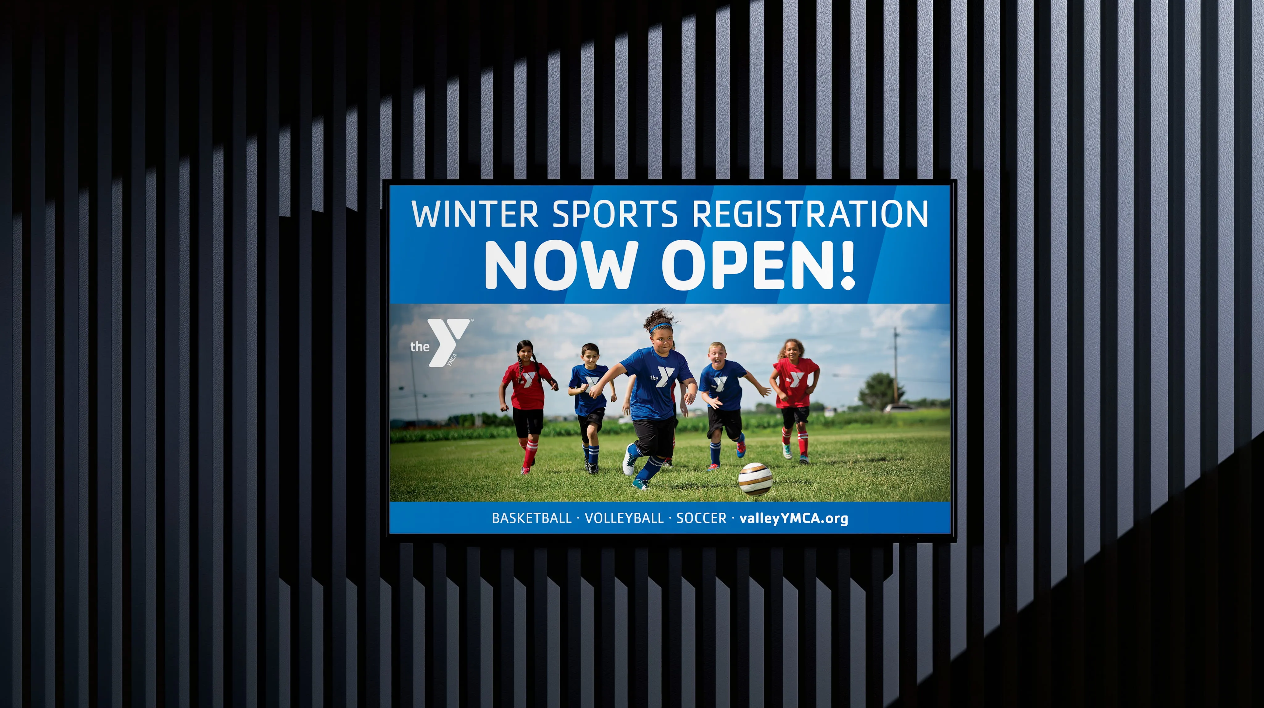 A screen on a dark wall showing a YMCA winter sports registration announcement.