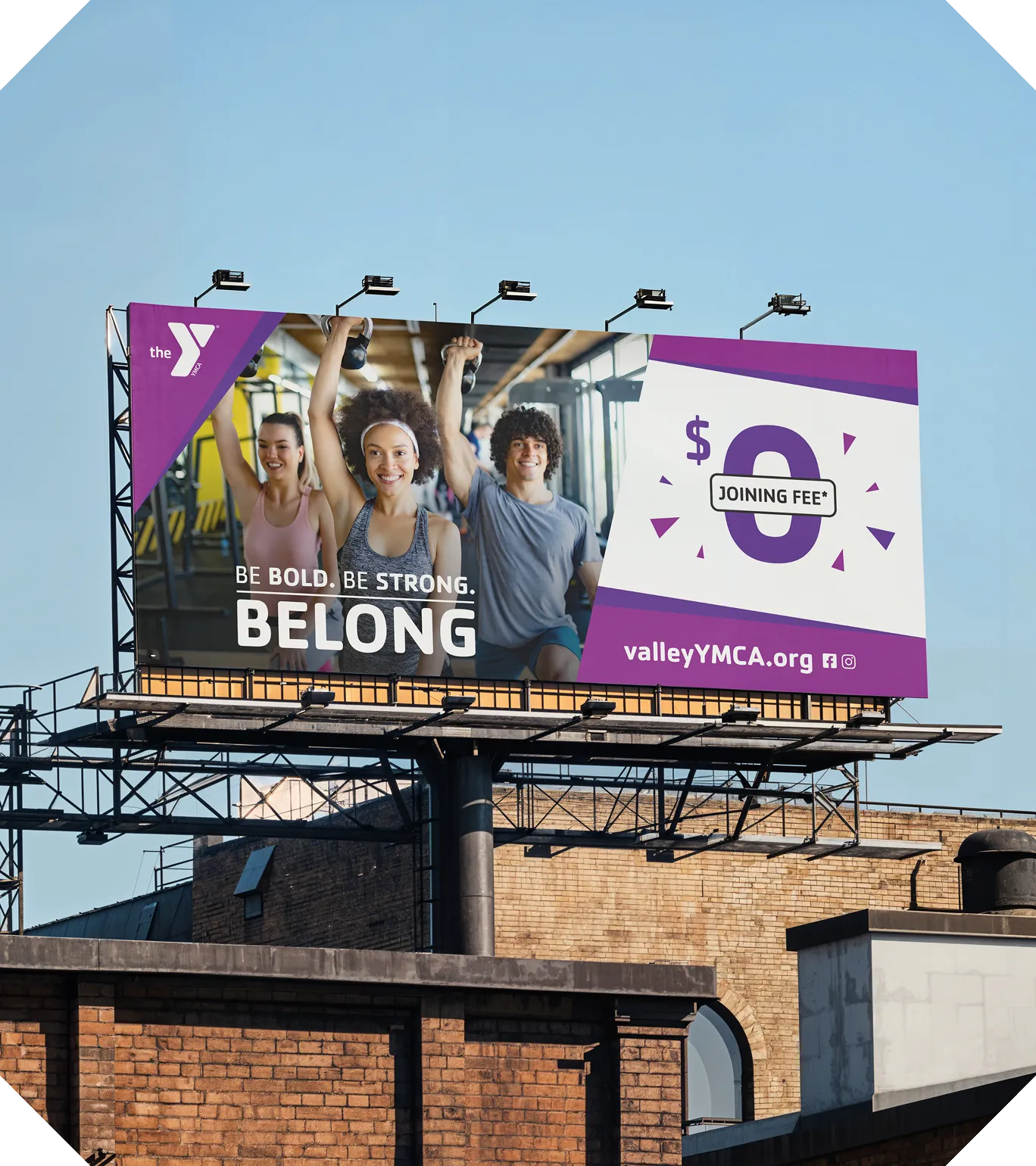 A YMCA "Be Bold. Be Strong. Belong." billboard above a brick building.