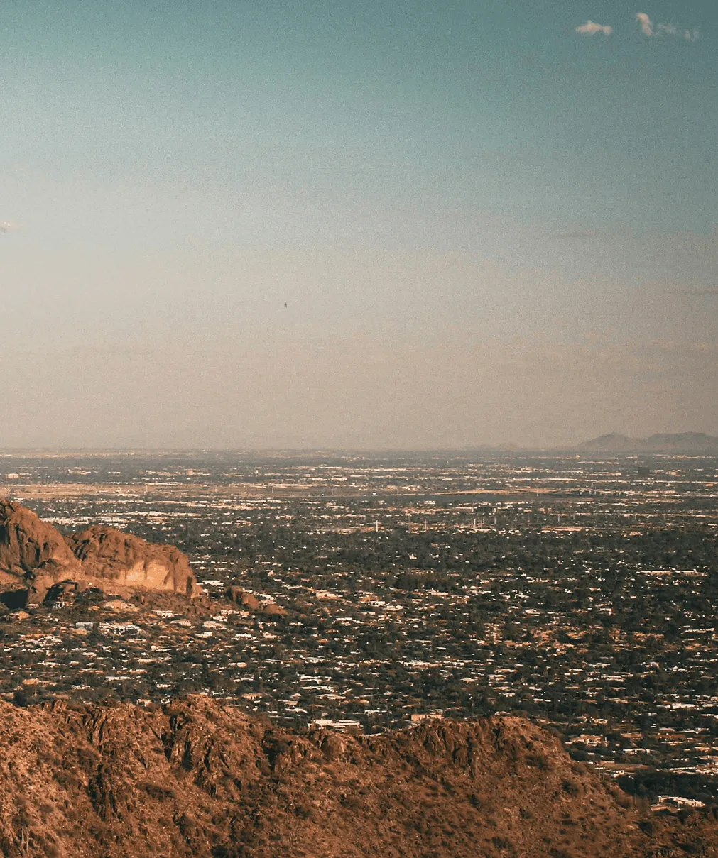 An aerial view of a desert city at dusk with rocky hills in the foreground.