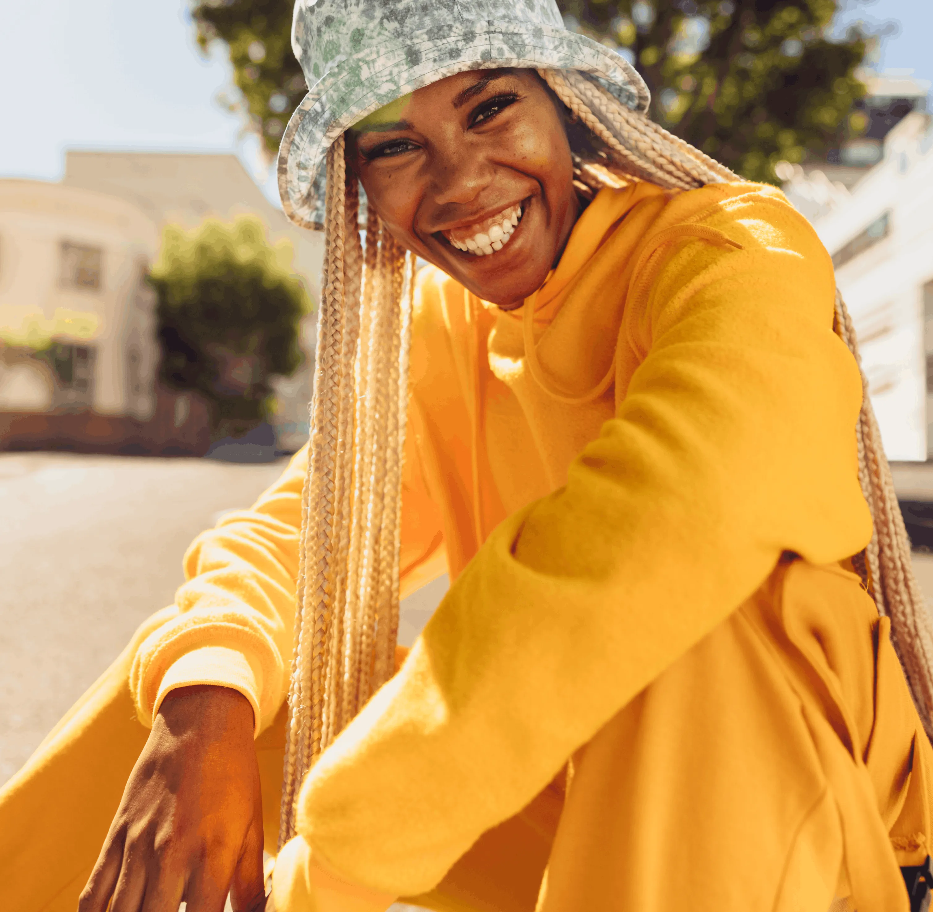 A woman in a yellow jacket and knitted hat smiling in bright sunlight.