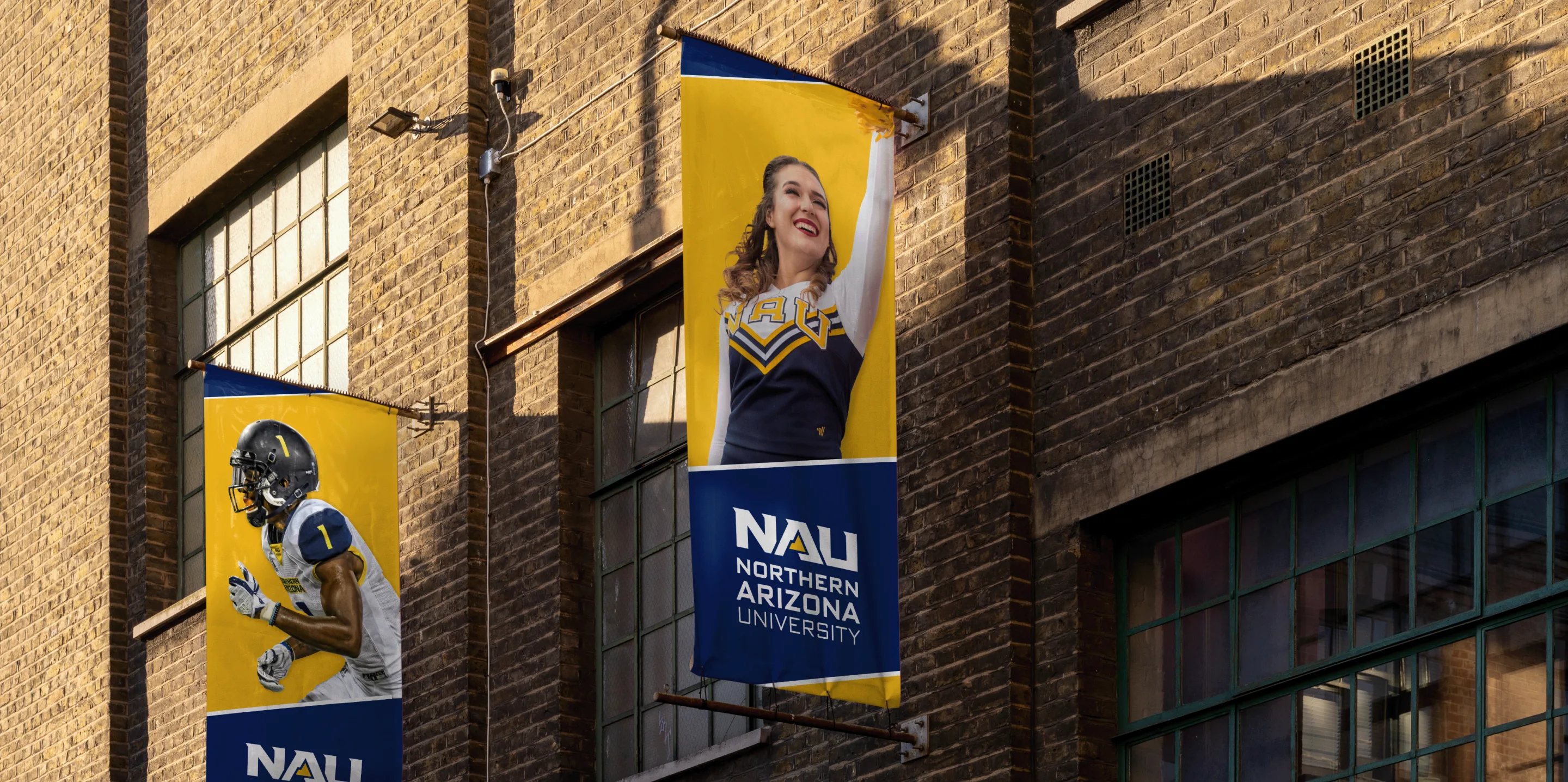 Two NAU banners on a brick building, showing a football player and a cheerleader.