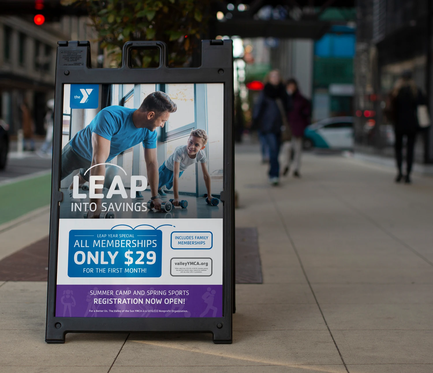 A YMCA "Leap into savings" pavement sign on a busy street.