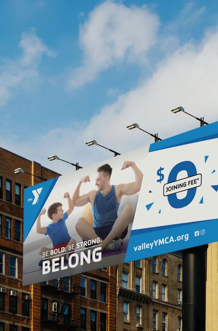 A YMCA billboard reading "Be Bold. Be Strong. Belong." with a $0 joining fee offer.