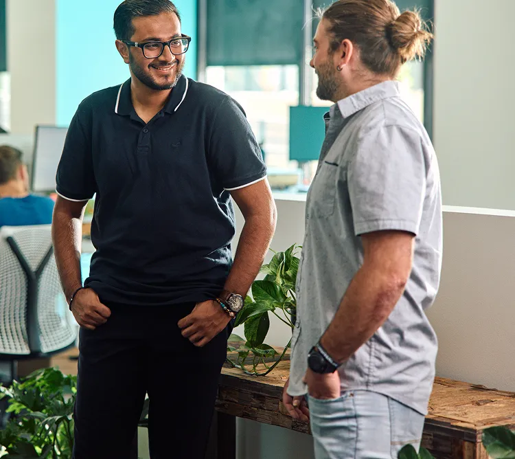 Two colleagues in Paradox polo shirts in conversation beside an office window.