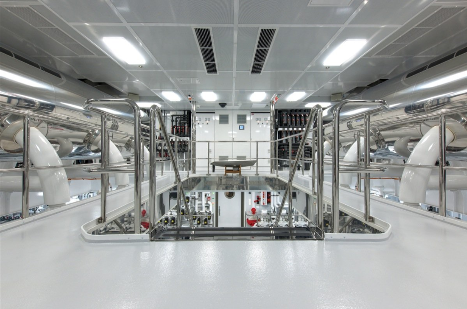 Interior of a modern industrial facility with white floors, stainless steel railings, large white pipes, control panels, and bright ceiling lights.
