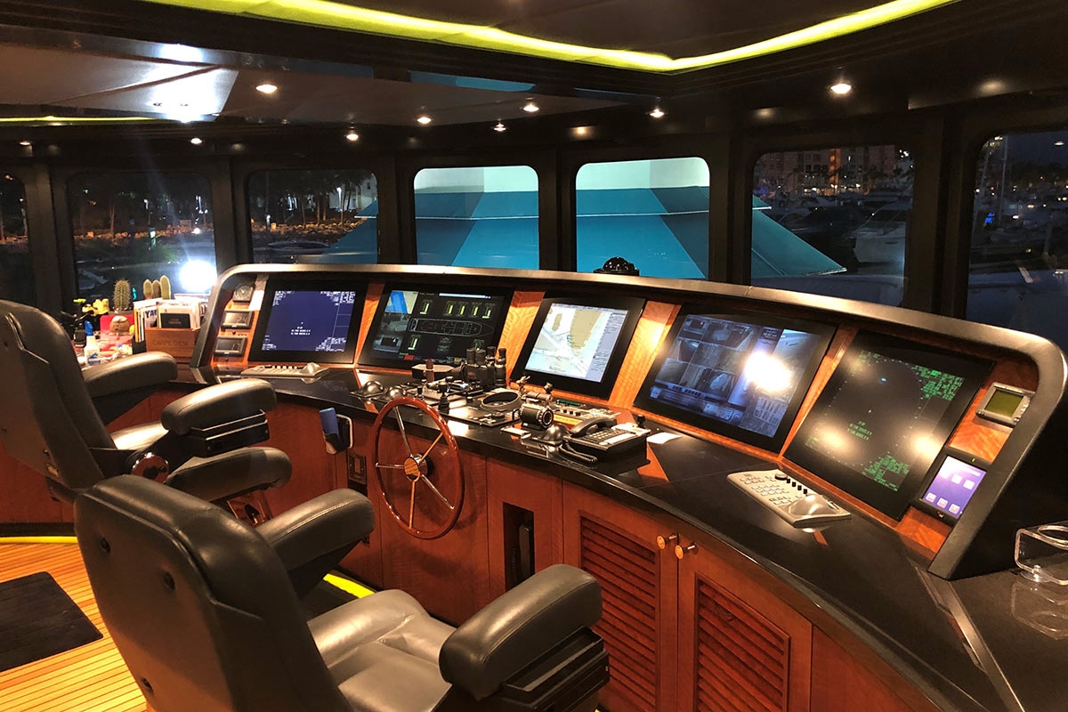 Luxurious yacht control room with leather chairs, wooden steering wheel, and multiple navigation screens at night.