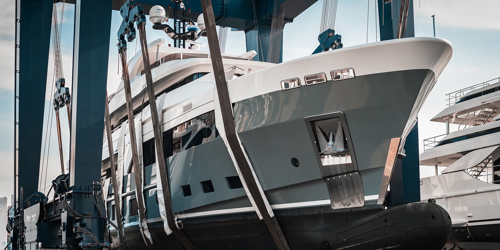 Large luxury yacht being lifted by a blue boat hoist at a marina.