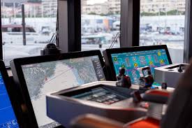 Ship bridge control panels with navigation and system screens displaying maps and data, overlooking a harbor.