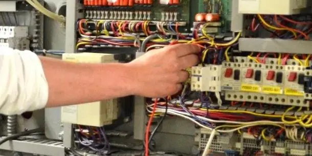 Person's hand working on electrical wiring inside an open control panel with multiple colored wires and components.