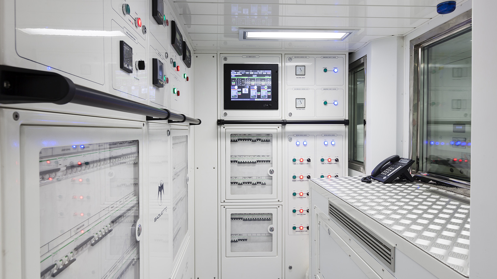 Interior of a modern control room with white panels, digital screens, buttons, switches, and a telephone on a metal counter.