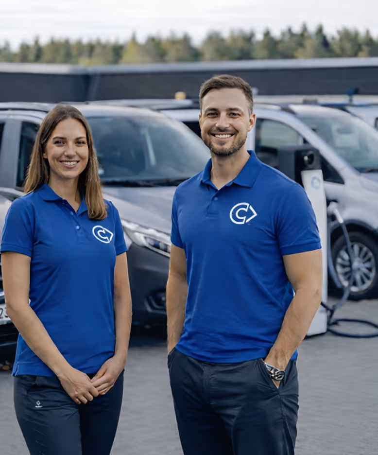 Zwei Personen in blauen Poloshirts stehen vor mehreren geparkten Autos an einer Ladestation.