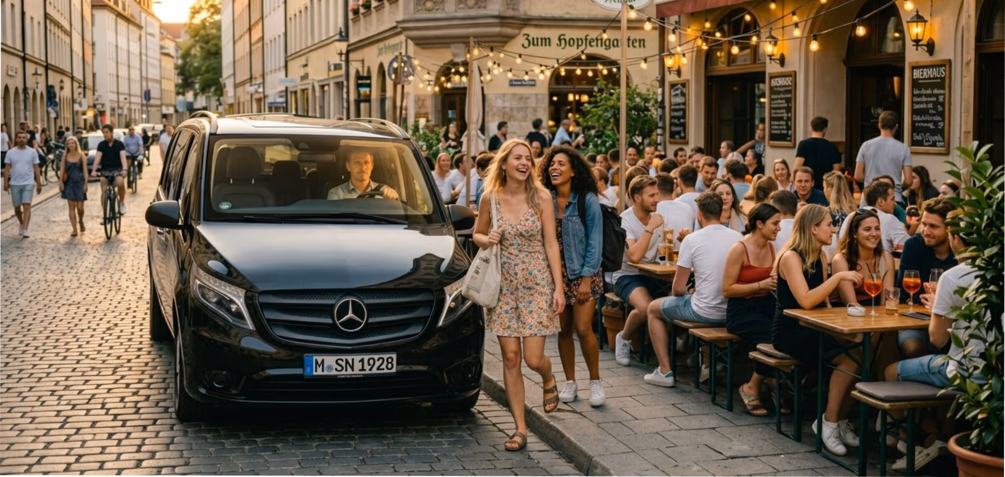 Zwei lachende Frauen gehen neben einem parkenden Mercedes vor einem belebten Straßenrestaurant.