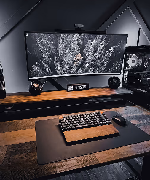 Minimalist PC setup with ultra-wide monitor showing snowy pine trees, keyboard, mouse, and digital clock.