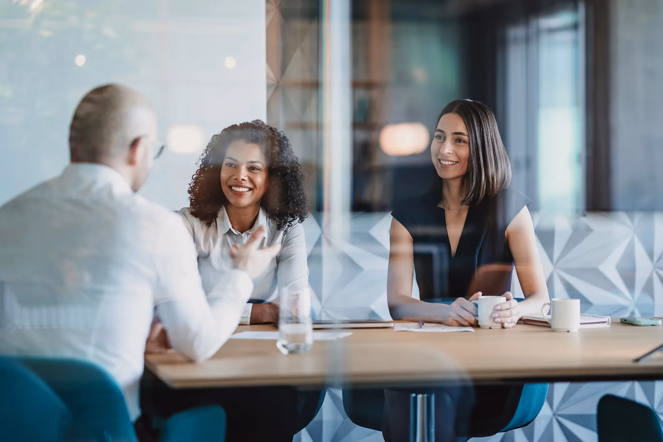 Two women and a man having a discussion at a conference table in a modern office. 