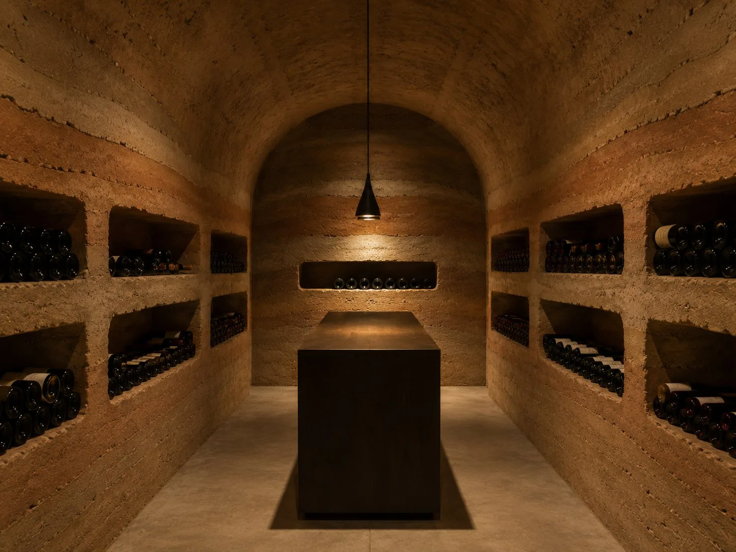 Dimly lit wine cellar with bottles stored in wall niches and a central table under a hanging lamp.