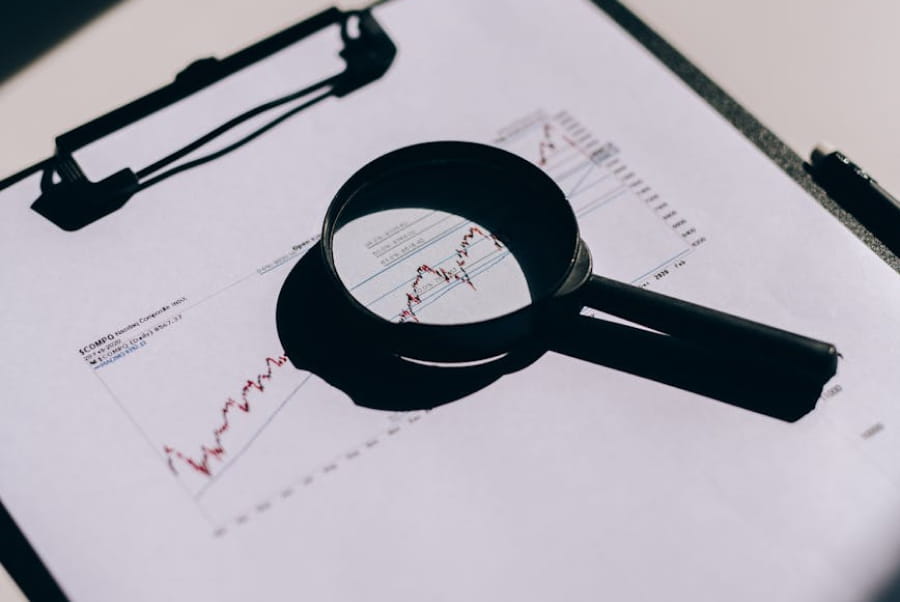 Magnifying glass on clipboard focusing on a rising stock market chart line graph.