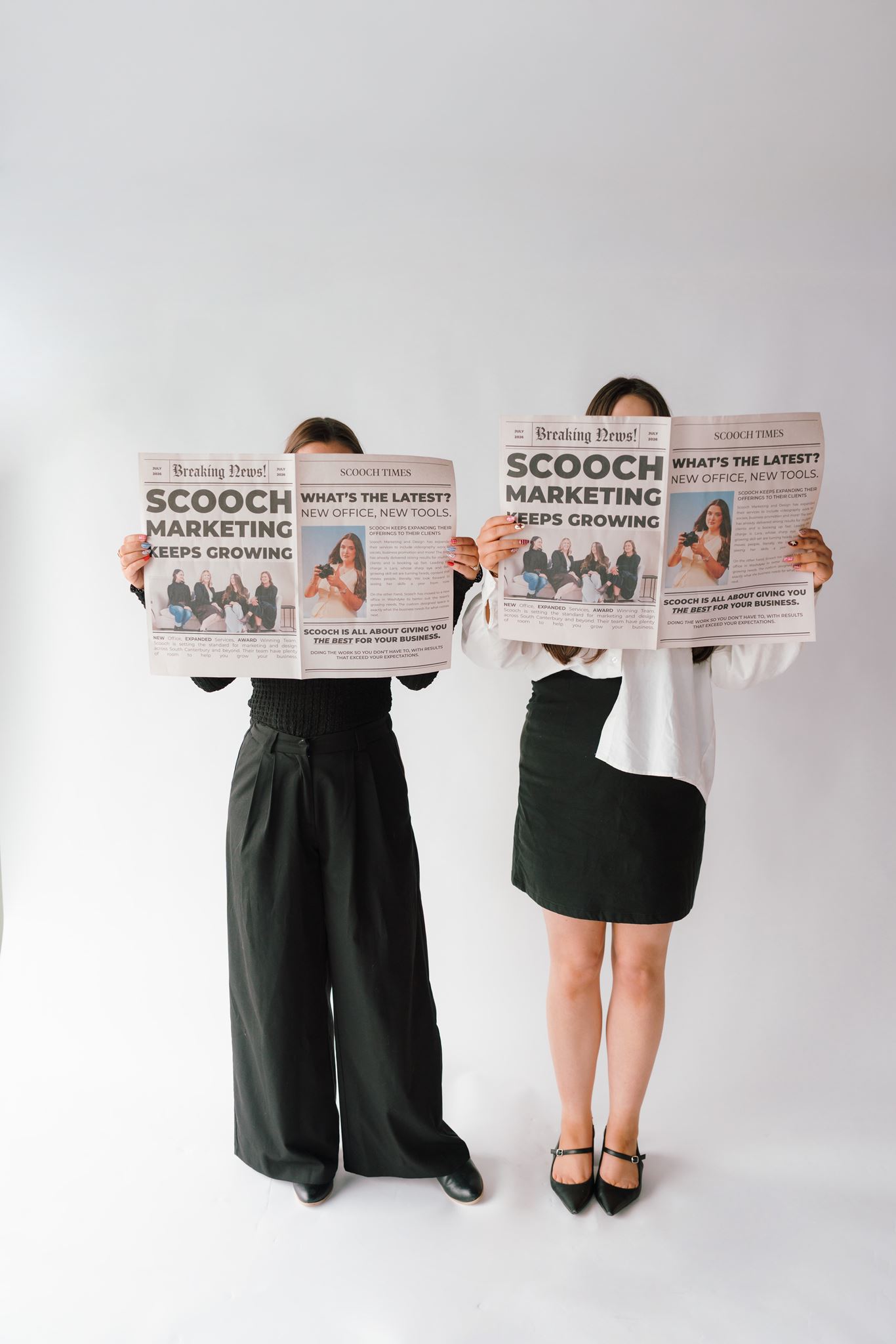 Sarah and Lara holding scooch newspapers in front of  their faces