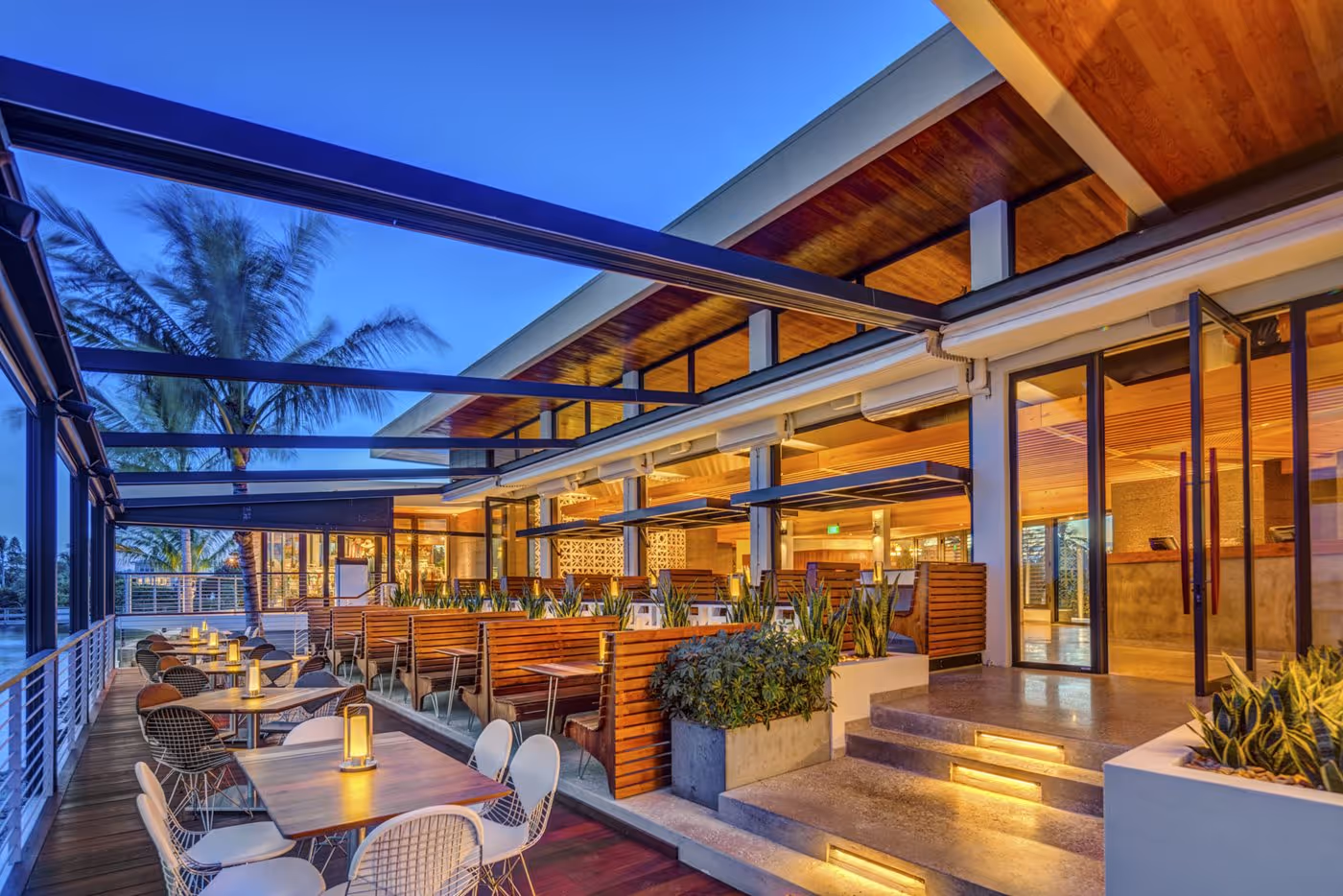Modern outdoor restaurant seating area at dusk with wooden booths, tables, and warm lighting.