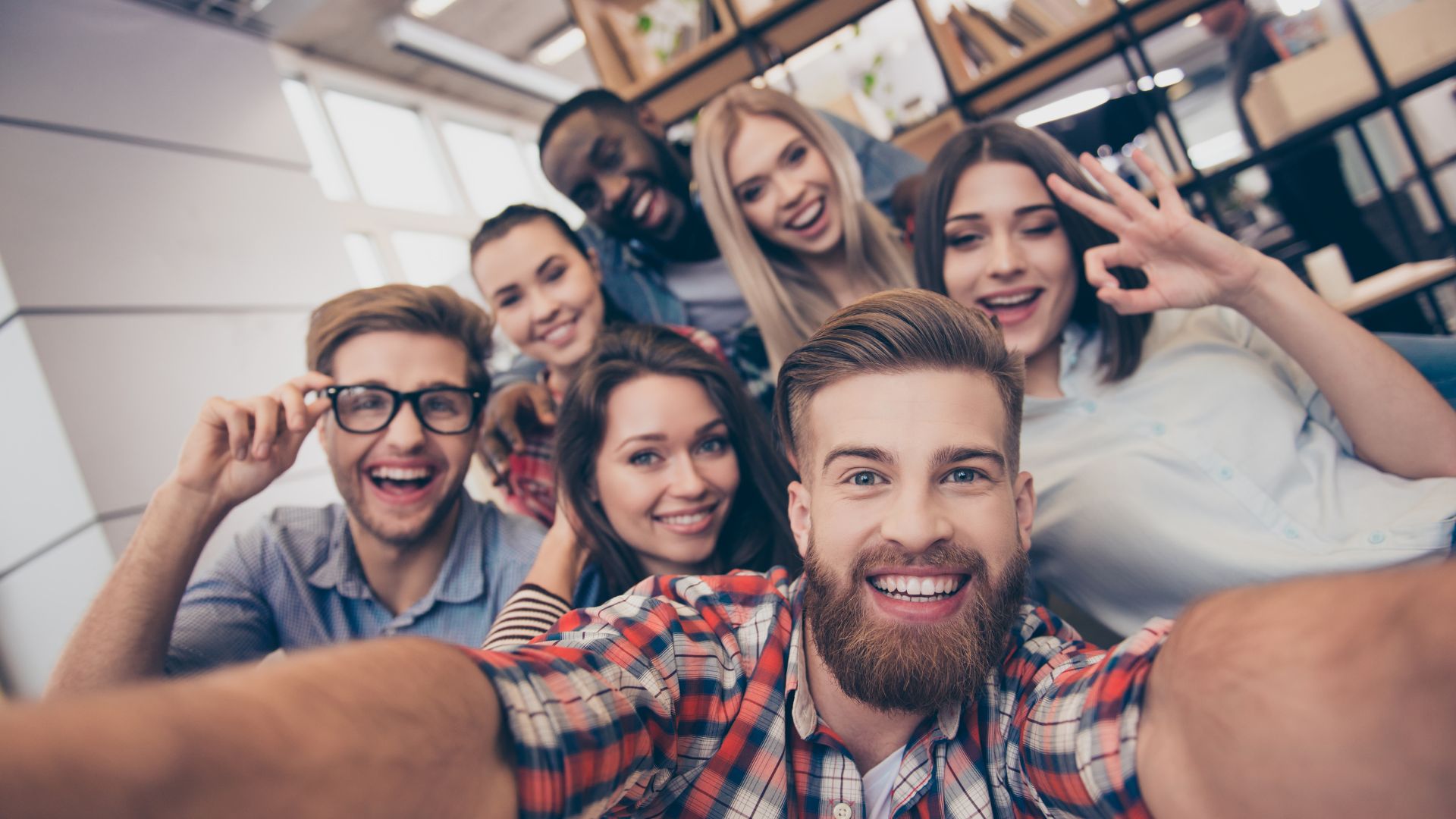 Gruppe von sieben lächelnden jungen Erwachsenen, die einen Selfie-Foto im Büro machen.