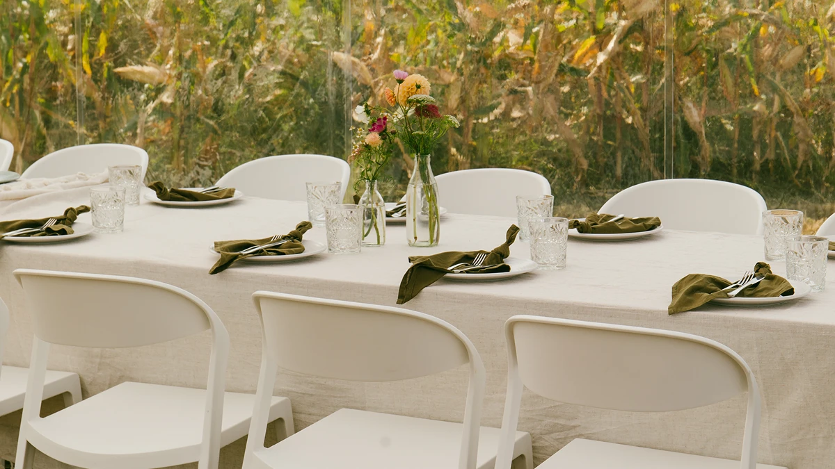 Table set with white chairs, glassware, olive green napkins, and small floral centerpieces.