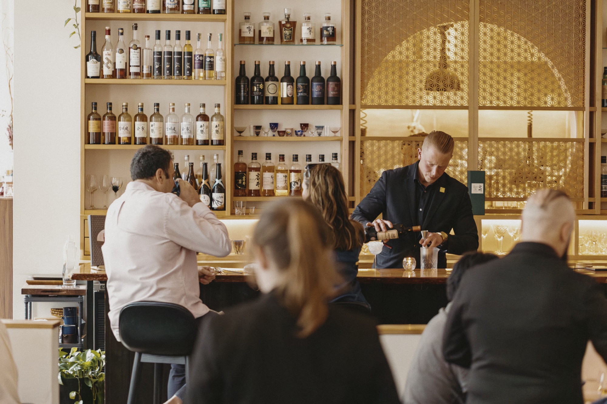 Bartender pouring a drink behind the whisky bar, shelves of Japanese whisky above