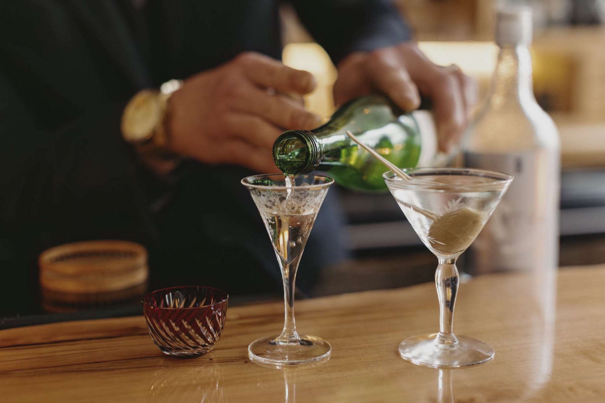 Sake poured from a green bottle into etched crystal glasses at the bar
