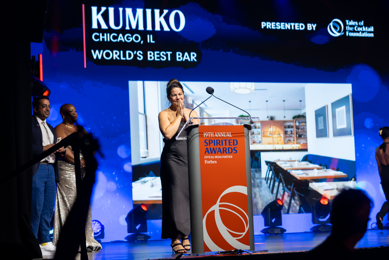 Julia Momosé onstage at the Spirited Awards as the screen behind her reads "Kumiko, Chicago, IL — World's Best Bar"