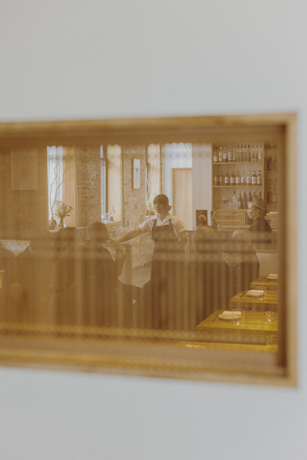 Julia Momosé in chef's whites, seen through an interior window into the Kumiko dining room