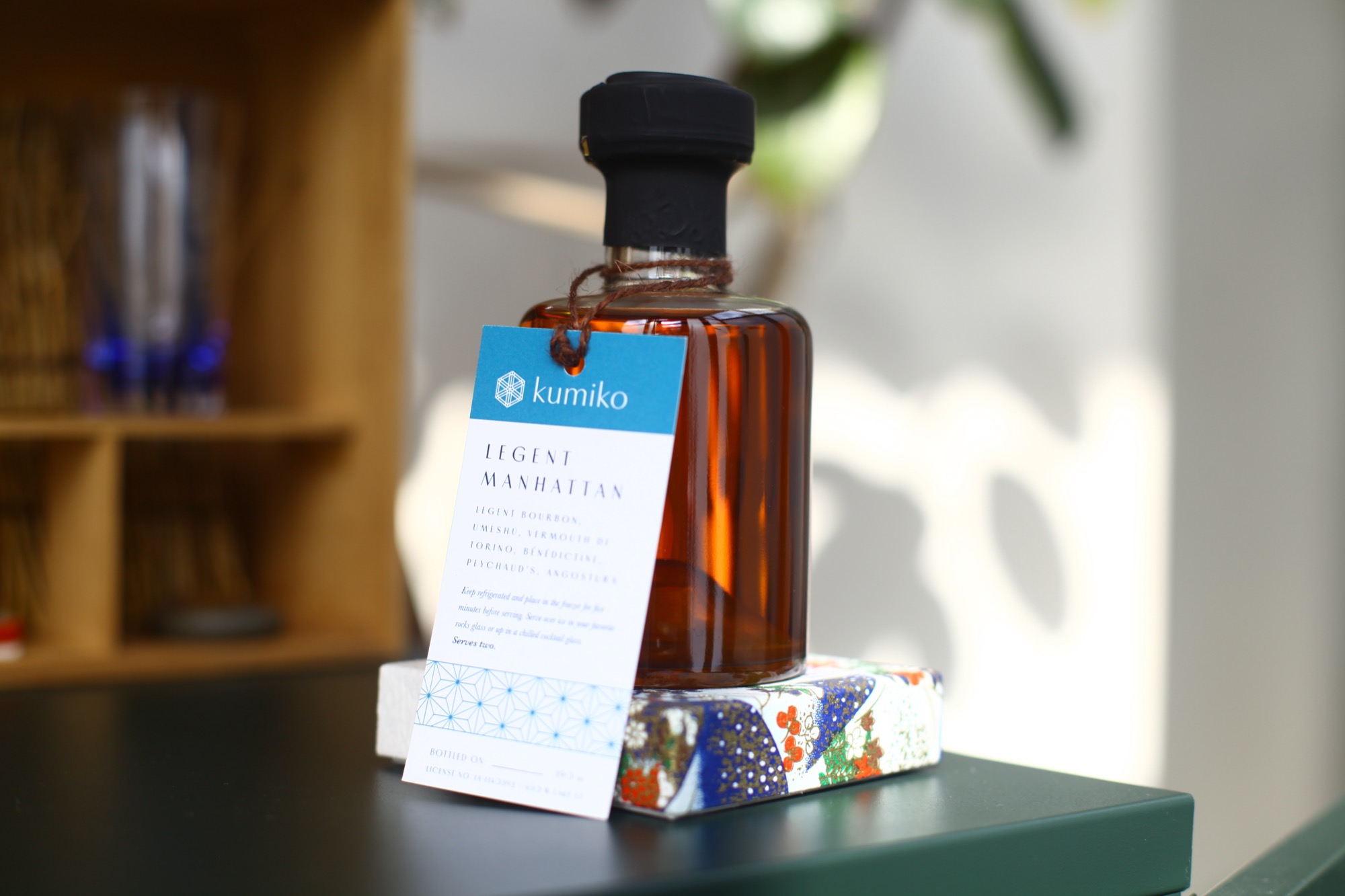 A bottled Legent Manhattan cocktail with a Kumiko tasting-note tag tied to its neck