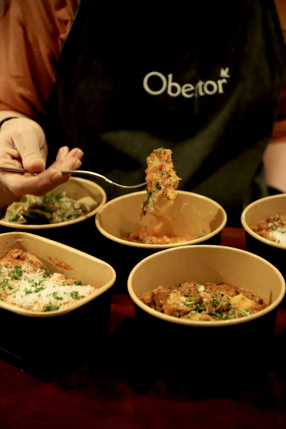 Obertor team member plating pasta, branded apron visible