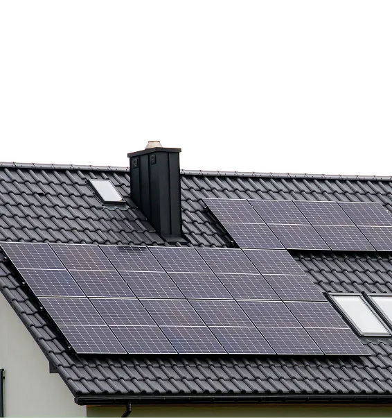 Hausdach mit installierten Solarpanels auf dunklen Ziegeln neben einem schwarzen Schornstein und zwei Dachfenstern.