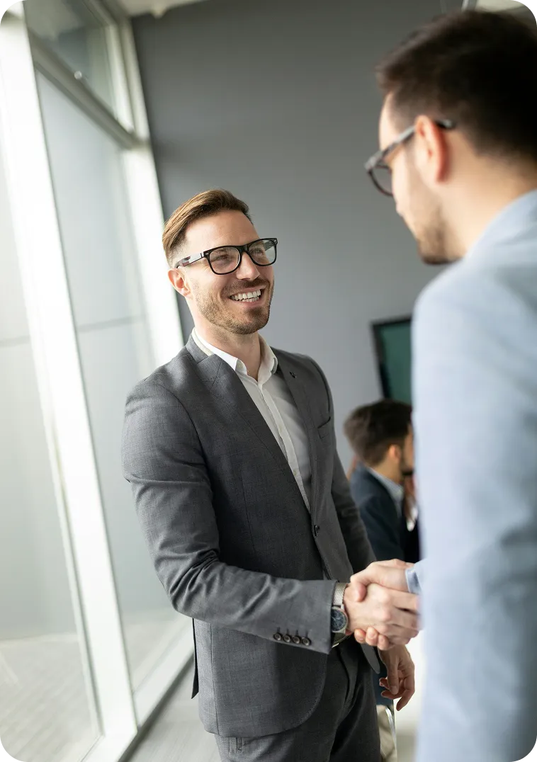 Zwei Geschäftsmänner schütteln sich lächelnd die Hand in einem modernen Büro.