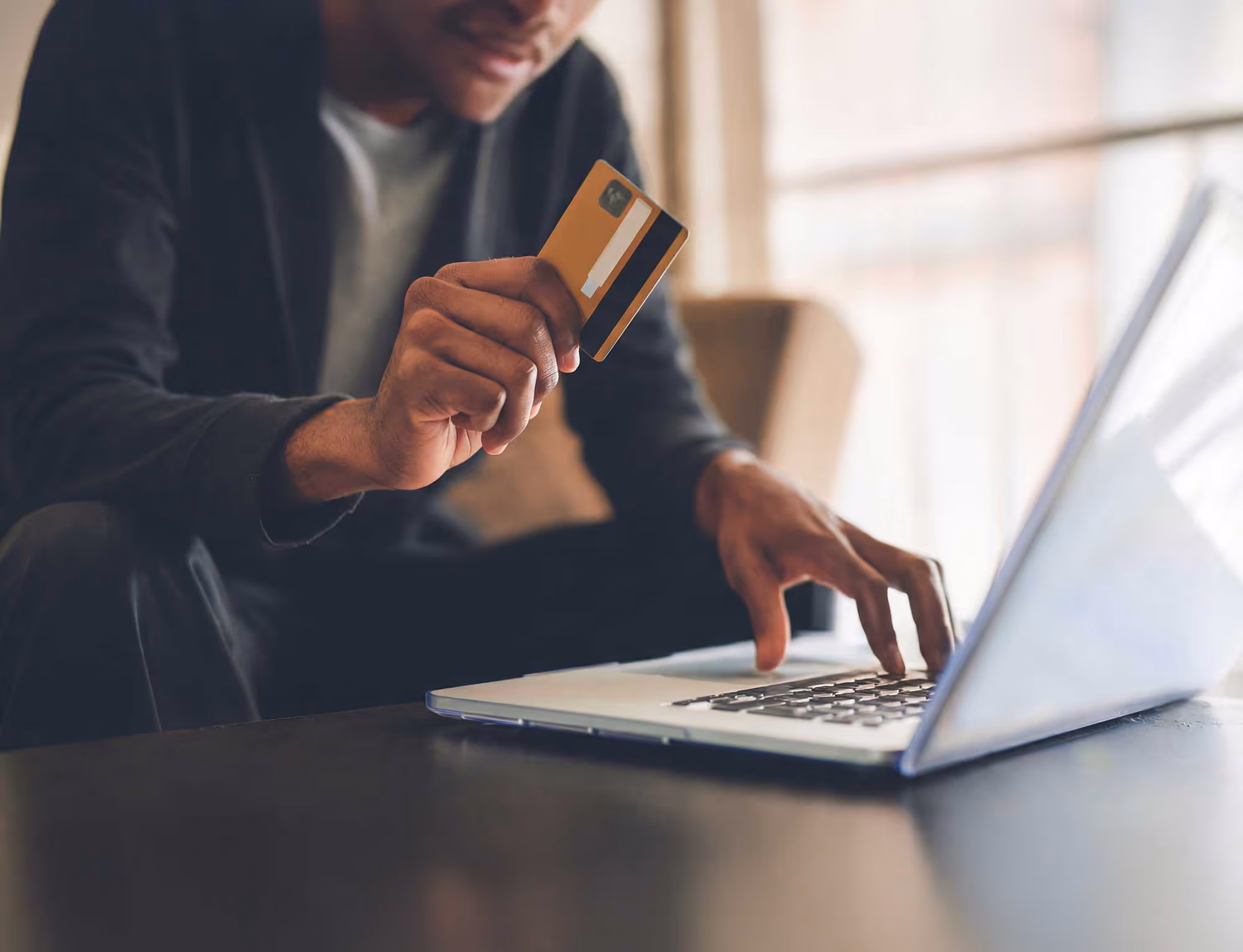 Person holding a credit card in one hand and typing on a laptop with the other, suggesting an online payment.