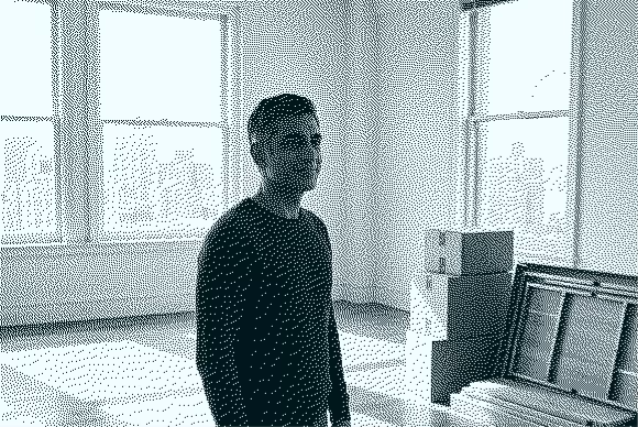 Man standing in an empty room with large windows and a stack of cardboard boxes nearby.