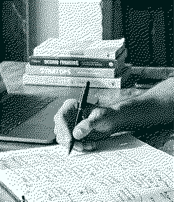 Hand holding a pen writing on paper with stacked books blurred in background.