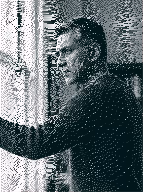 Man with short hair looking out a window with a thoughtful expression.