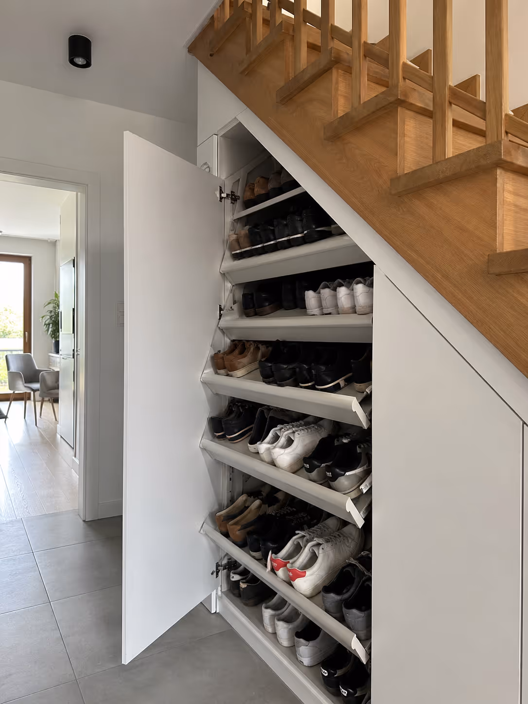 Zabudowa pod schodami na buty — wyciągane półki, biały laminat, dom