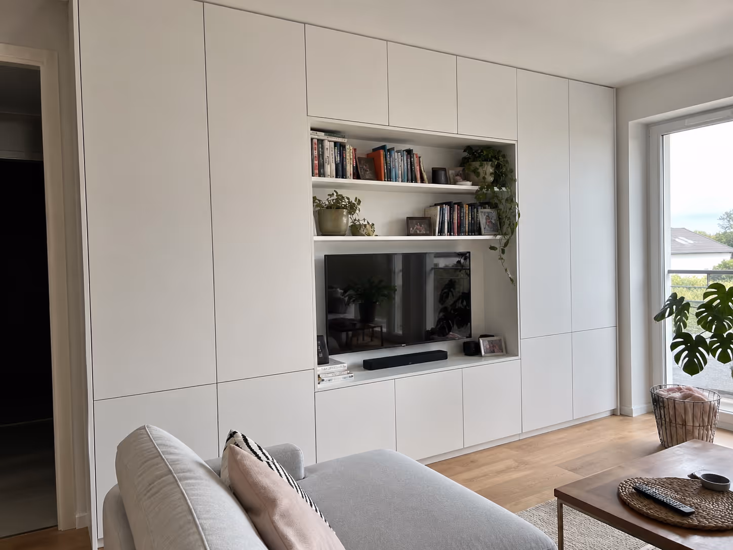 Zabudowa całej ściany w salonie na wymiar Wrocław — biały mat, miejsce na TV, regały LDSP