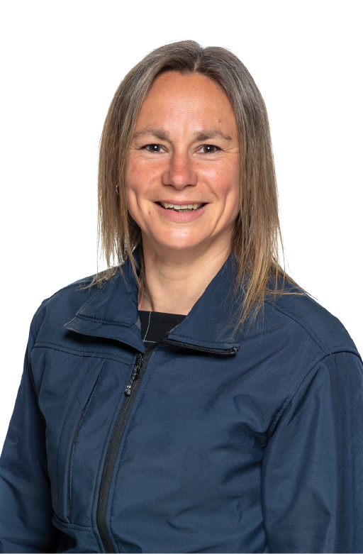 Smiling woman with straight grey-brown hair wearing a dark blue zip-up jacket over a black top, against a white background.