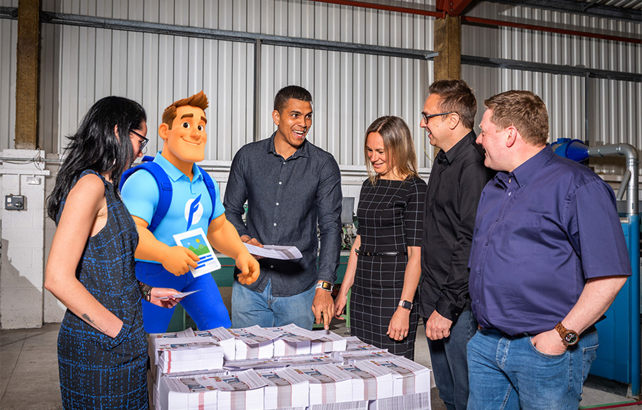 Five people, including one animated character in blue with a backpack, stand around stacks of papers or flyers in an industrial setting, appearing to discuss or review the materials.