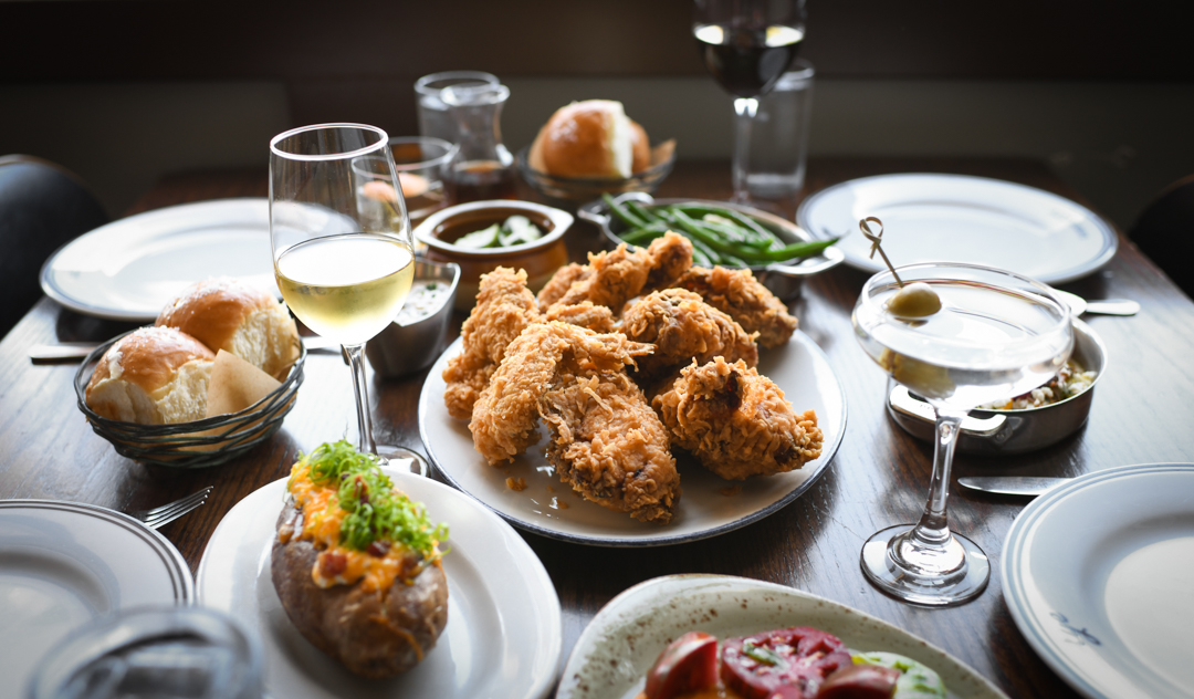 A table full of food and drinks with a glass of wine.