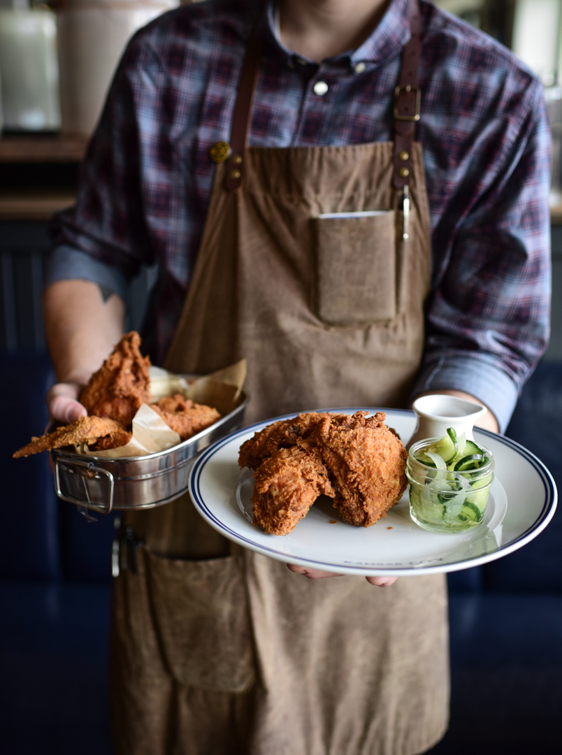 A man holding a plate with fried chicken and pickles.