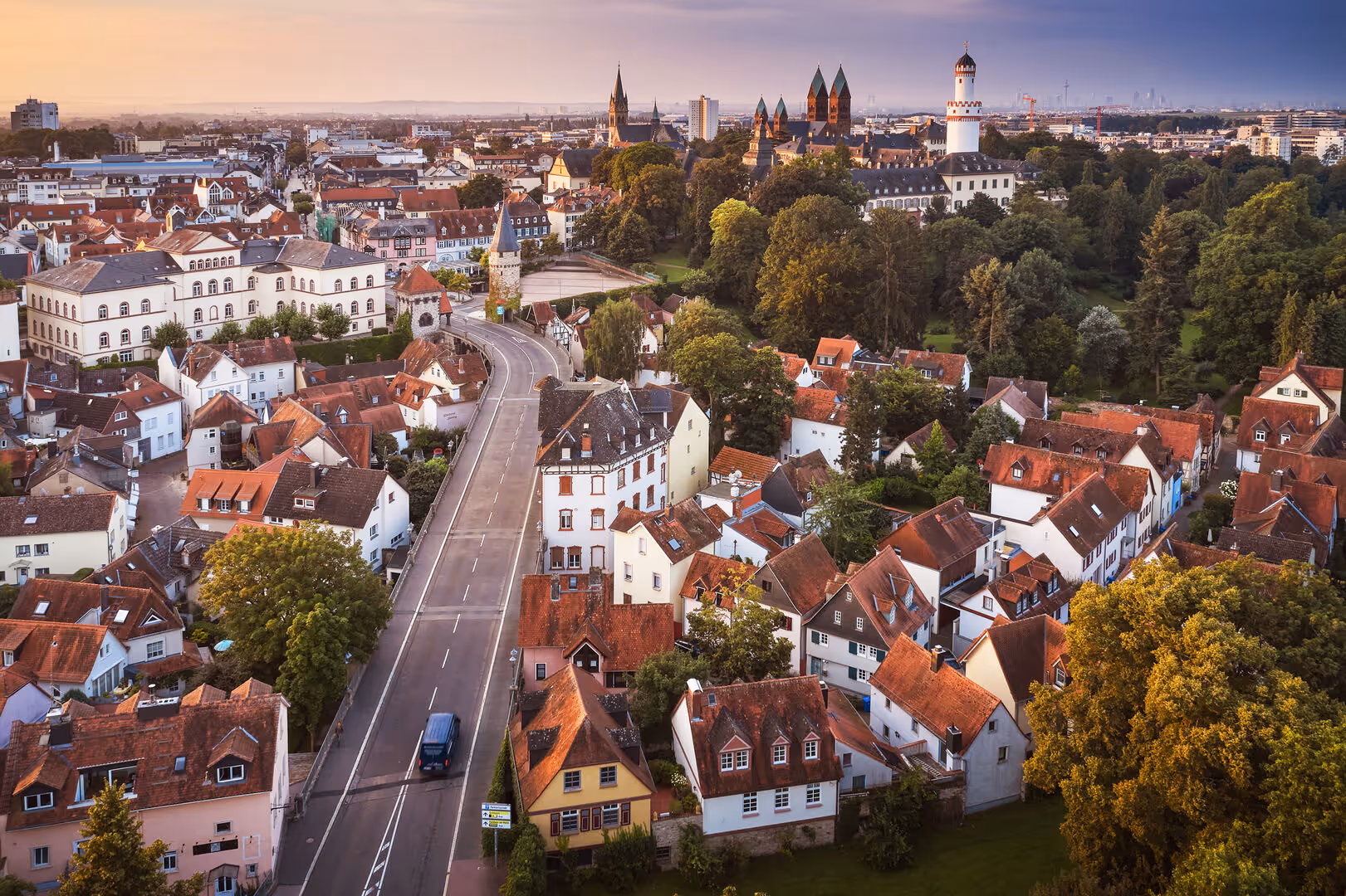 Luftaufnahme einer Altstadt mit roten Dächern, einer Straße und einem weißen Turm bei Sonnenuntergang.