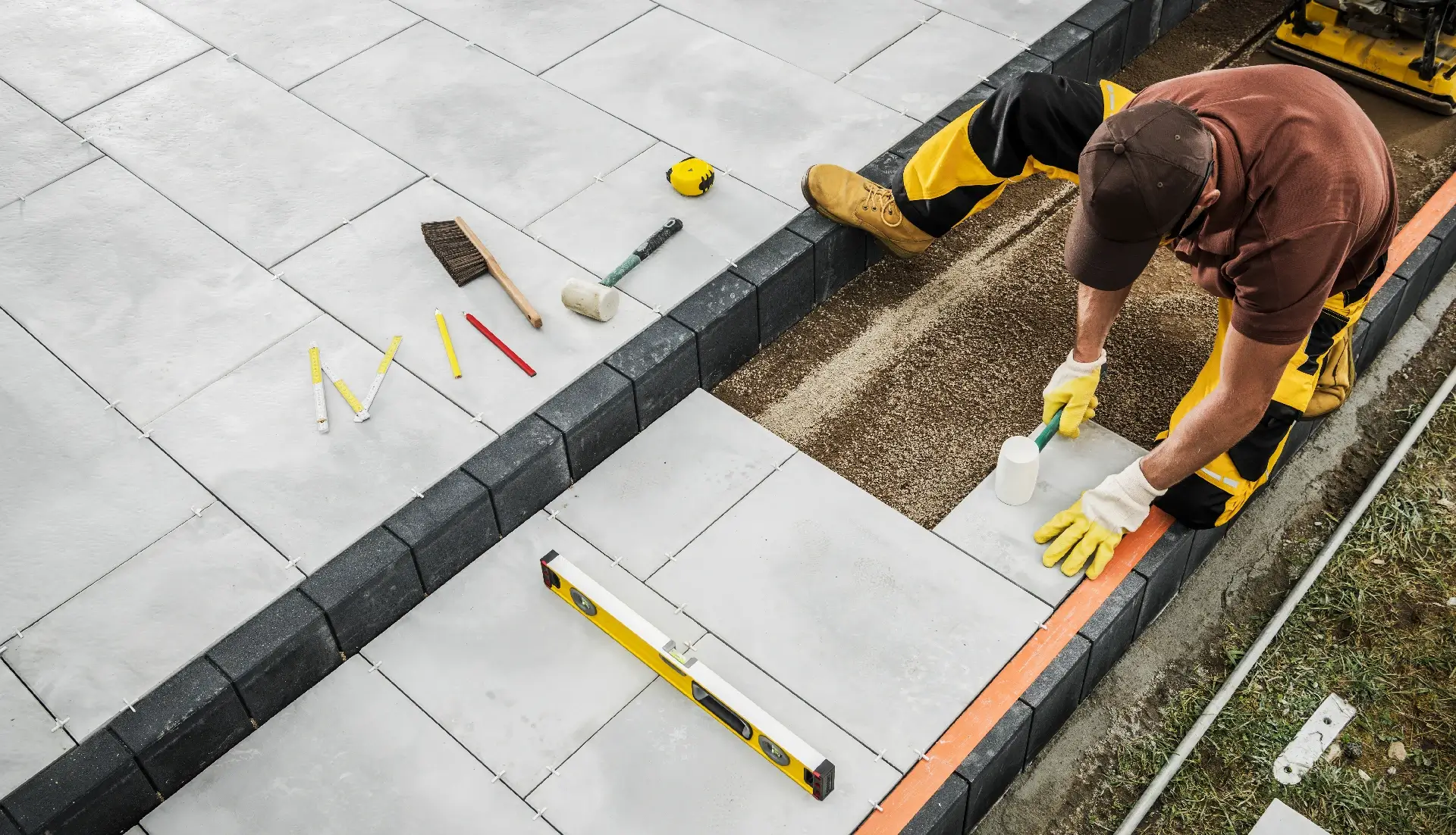 A skilled contractor is carefully positioning pavers in a backyard patio area, using tools like a level and measuring tape to ensure precision in the installation process.