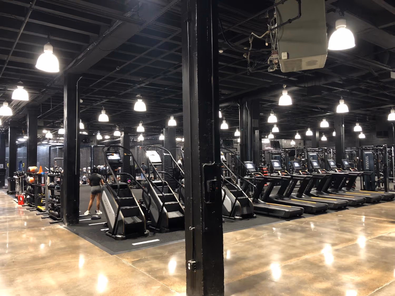 Modern gym with stair-steppers, treadmills, free weights, and a person exercising.
