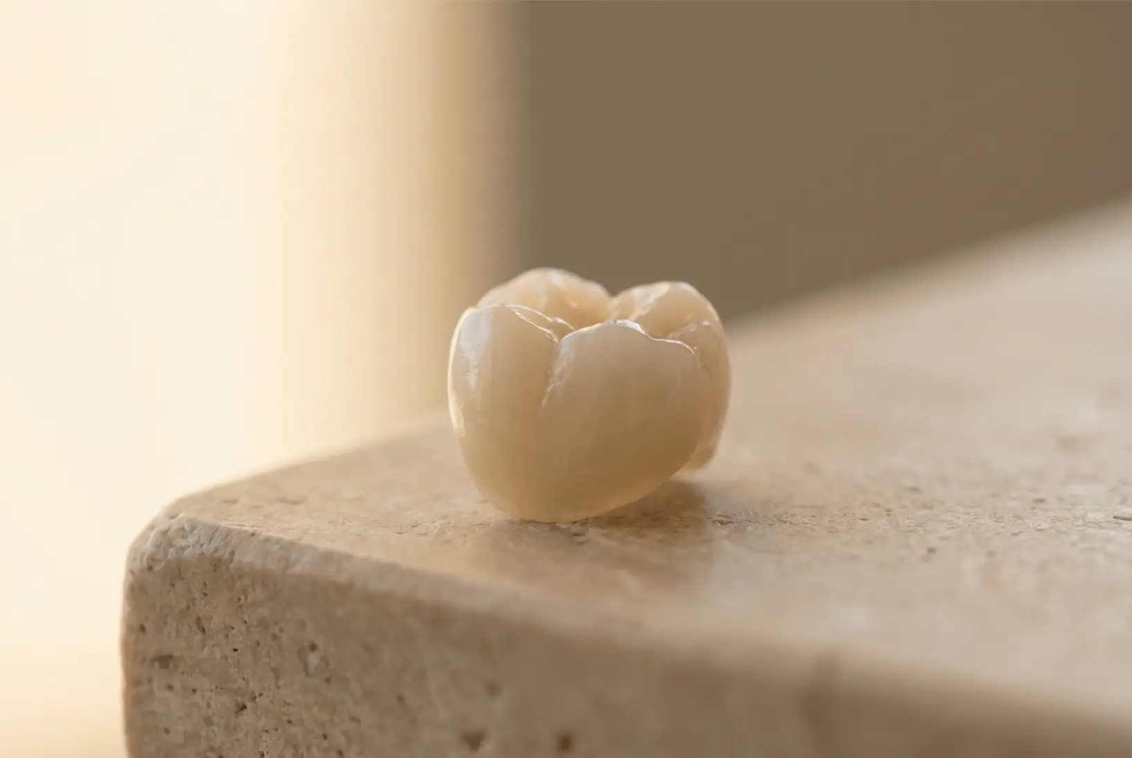 Close-up of a dental crown resting on a beige stone surface with soft lighting.
