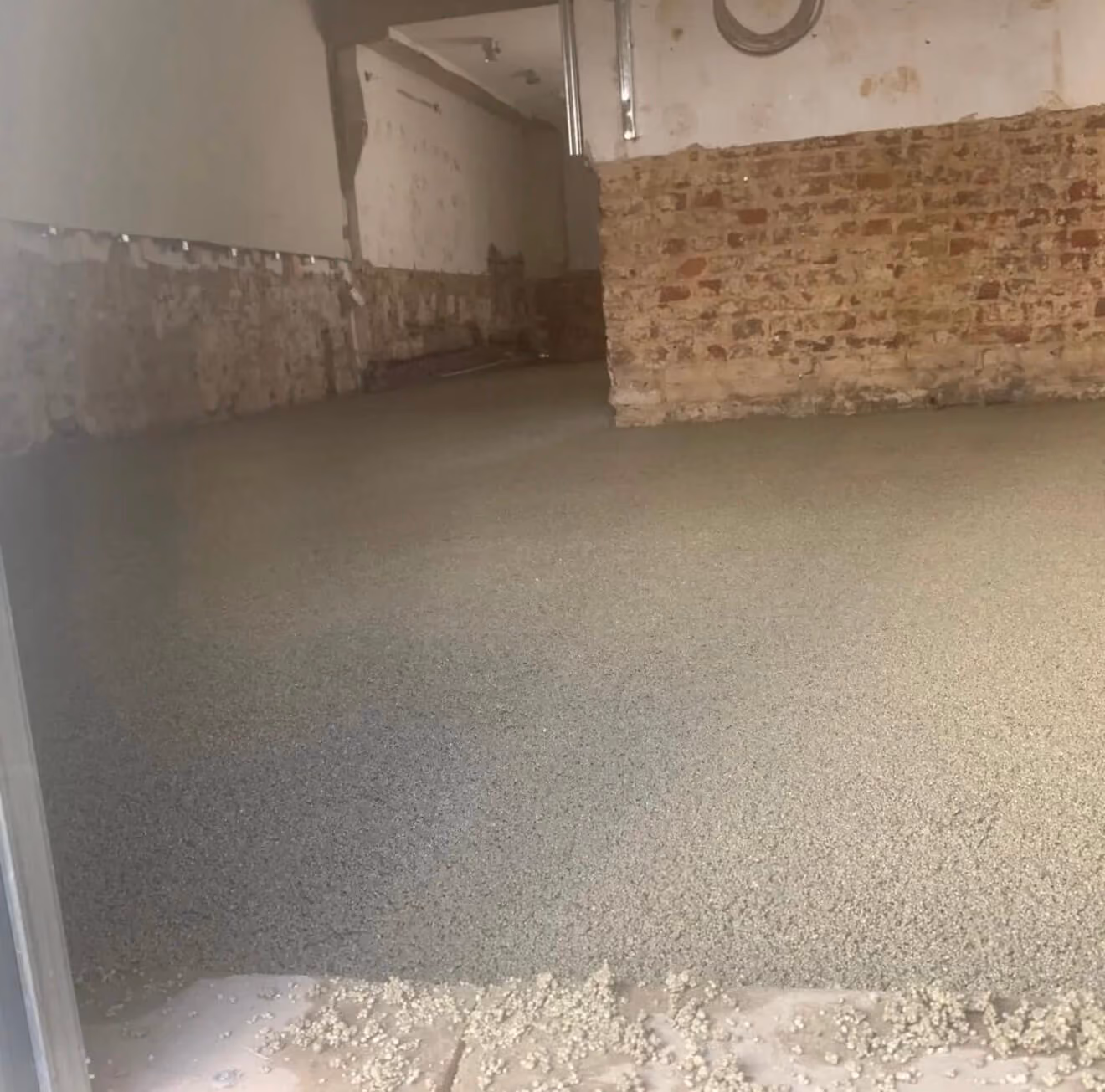 Boden mit frisch verteiltem Estrich in einem Raum mit teilweise freigelegten Backsteinwänden.